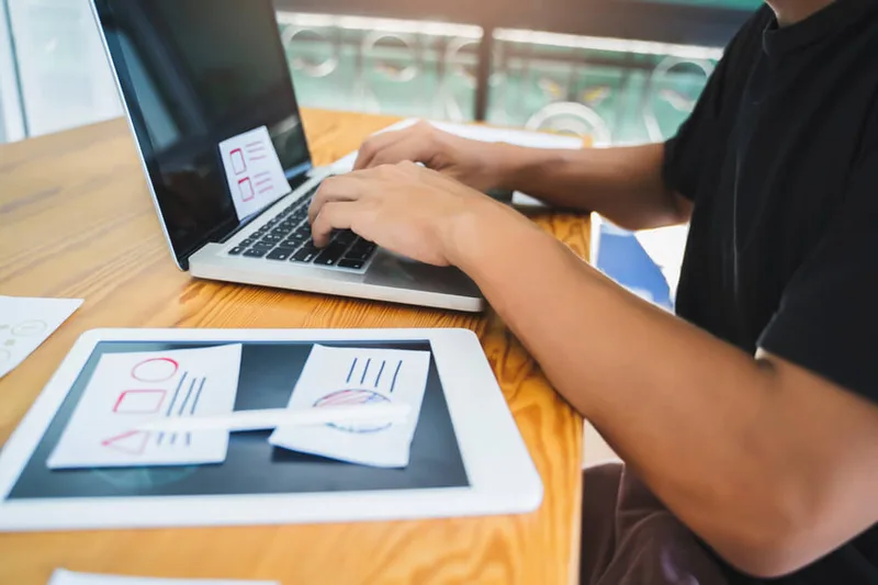 Web designer building a website layout on a laptop with design sketches nearby